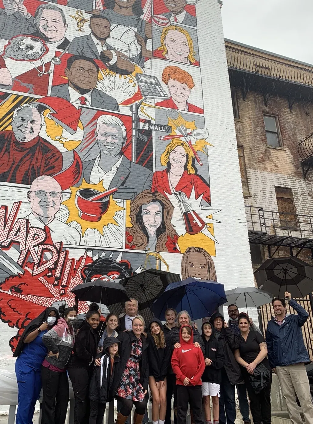 Dr. Oberlander with a group under umbrellas in front of a large painted mural